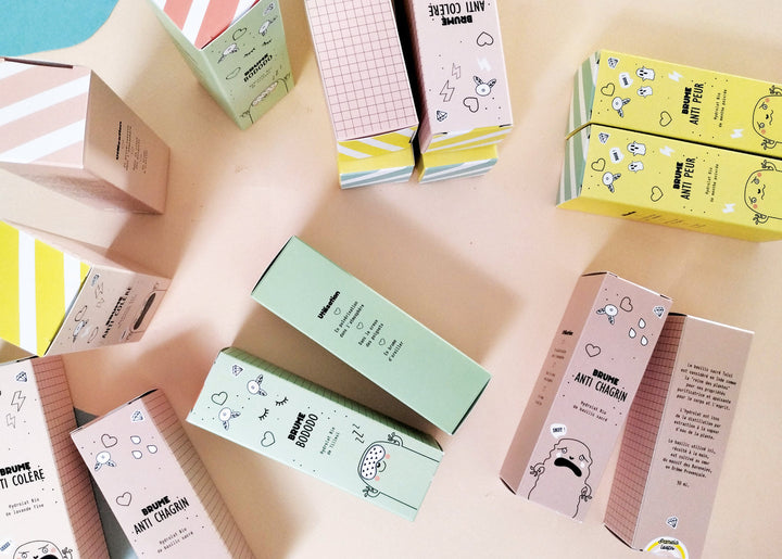 Collection des brumes pour les émotions Pamela Loops, boîtes colorées disposées à plat sur un fond rose pastel