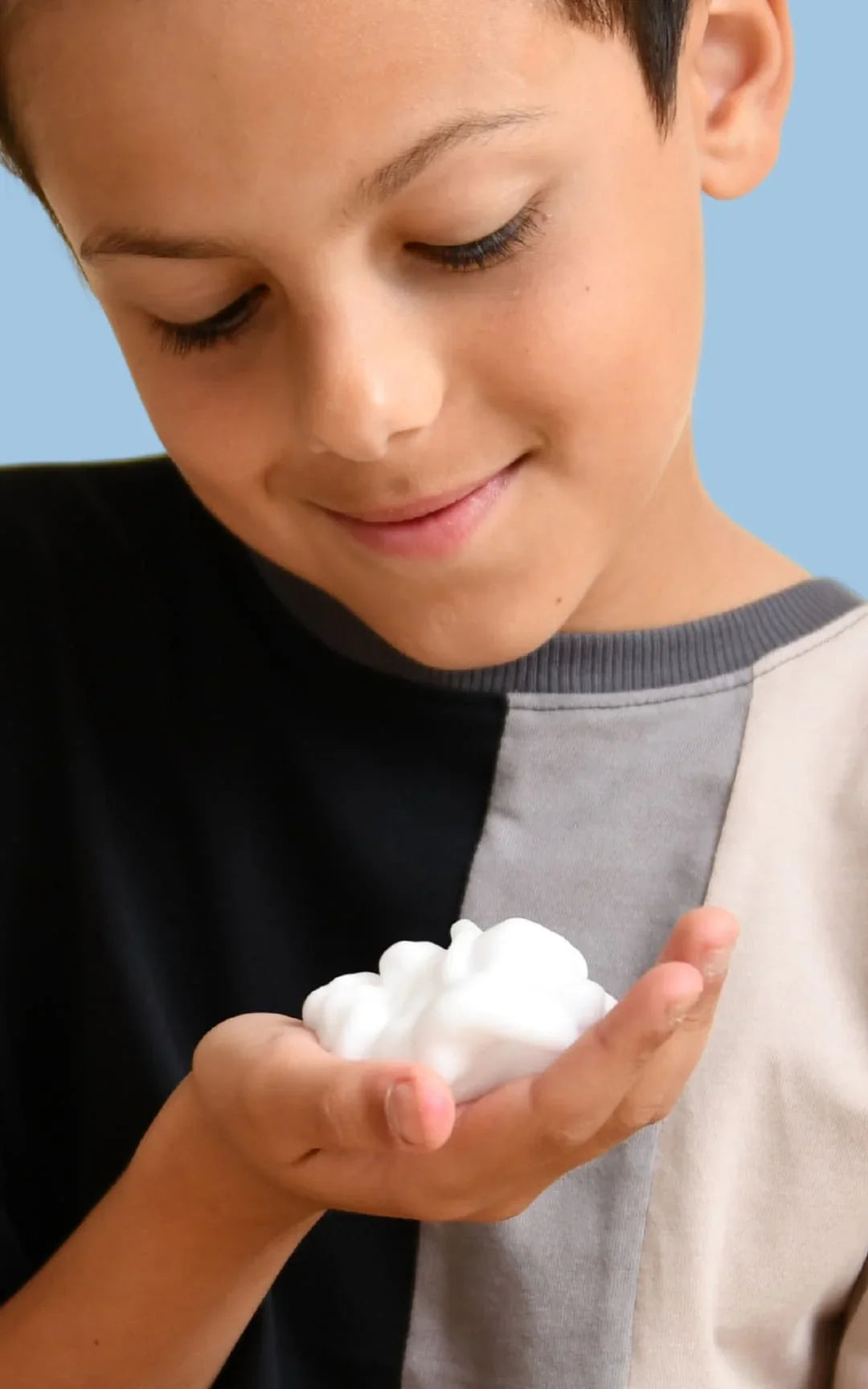 Jeune garçon souriant jouant avec la mousse d'un bain moussant dans ses mains