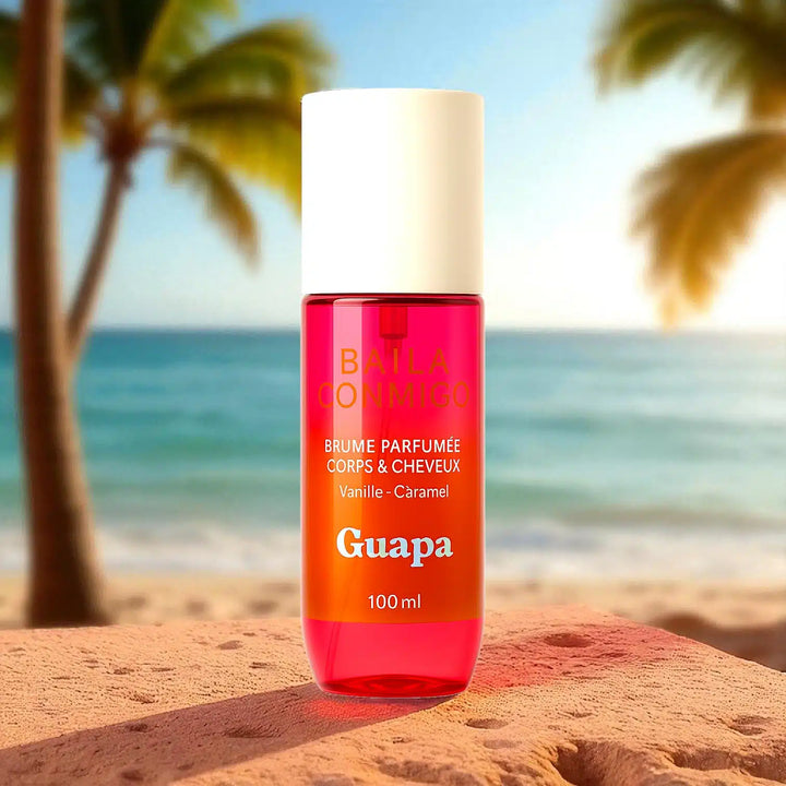 Brume parfumée Guapa vanille caramel posée sur un rocher devant une plage tropicale ensoleillée